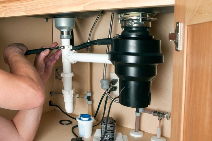 Plumber installing a garbage disposal beneath a kitchen sink in Venice